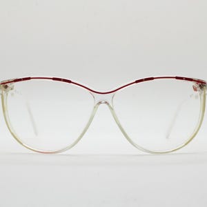 Könnte beinhalten: Transparente Cat-Eye-Brille mit rotem Metallrahmen.