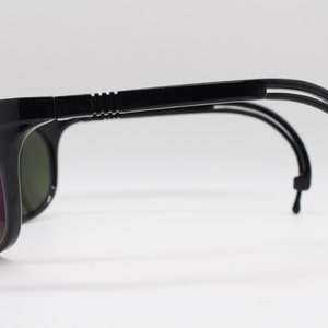 Puede incluir: Gafas de sol negras con un diseño envolvente y un sistema de doble brazo. Los brazos son flexibles y tienen una punta de goma negra.