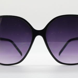 Puede incluir: Gafas de sol negras de gran tama&ntilde;o con montura cuadrada y lentes de color morado oscuro.