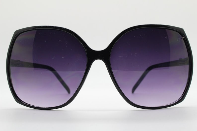 Puede incluir: Gafas de sol negras de gran tama&ntilde;o con montura cuadrada y lentes de color morado oscuro.