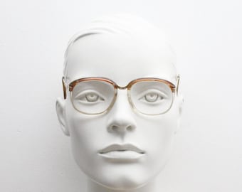 Puede incluir: Un par de gafas de pasta marrón y dorada con lentes transparentes. Las gafas están en una cabeza de maniquí blanca.