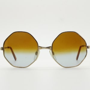 May include: Vintage octagonal sunglasses with a gold-tone frame and gradient lenses. The lenses transition from amber to blue. A stylish accessory for eye protection. The frame is made of metal.