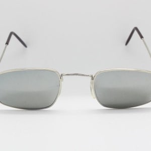 Peut inclure: Lunettes de soleil à monture argentée avec des verres miroir. La monture est fine et rectangulaire.