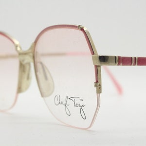 Könnte beinhalten: Rosa- und goldfarbene Brille mit geometrischem Gestell und der Signatur "Cheryl Tiegs" auf der rechten Linse.