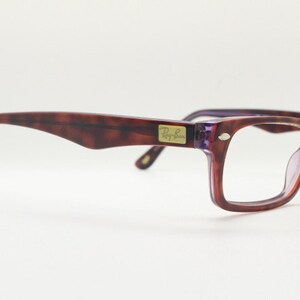 May include: A pair of tortoiseshell eyeglasses with purple frames and clear lenses. The Ray-Ban logo is visible on the right temple.