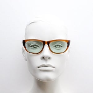May include: A white mannequin head wearing brown tortoiseshell cat-eye glasses with light green lenses.
