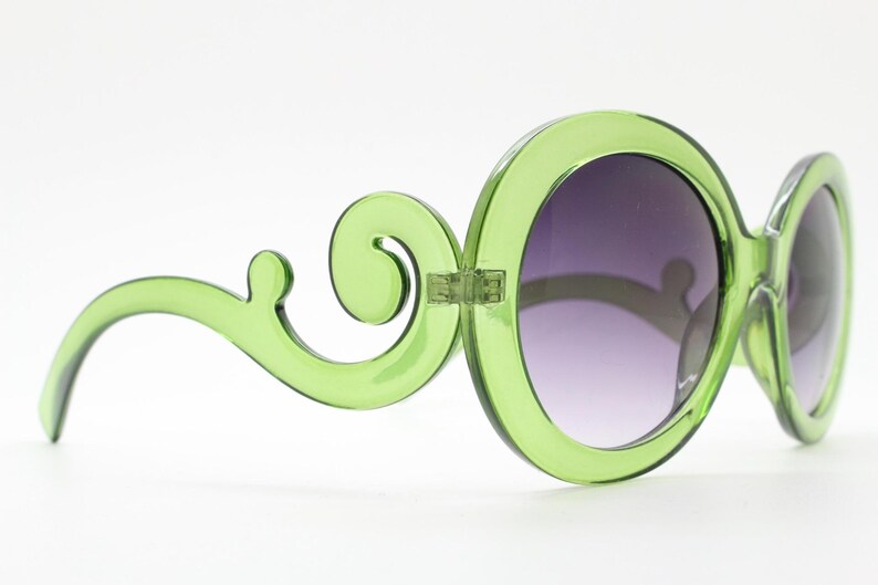 May include: Lime green sunglasses featuring large, circular frames and distinctive, swirling, scroll-like arms. The lenses are dark and have a gradient tint, transitioning from a darker shade at the top to a lighter shade at the bottom.