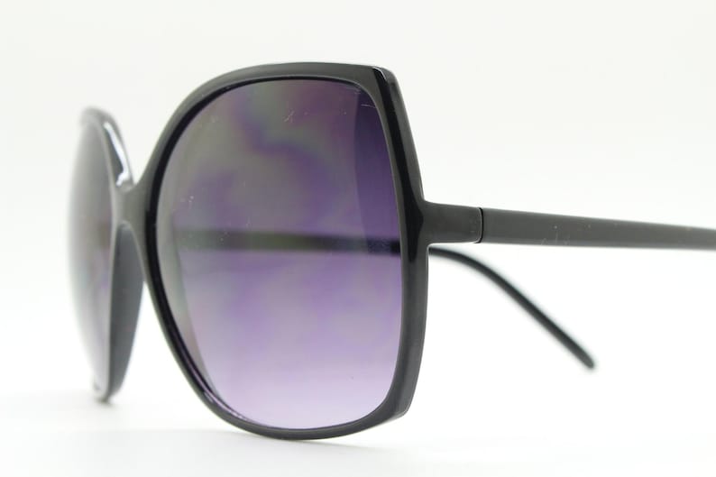 Puede incluir: Gafas de sol negras de gran tama&ntilde;o con montura cuadrada y lentes de color morado oscuro.