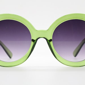 May include: Oversized round sunglasses featuring a translucent lime green plastic frame and dark gradient lenses that transition from a deep purple tint at the top to a lighter shade at the bottom, with visible hinges on the outer edges.