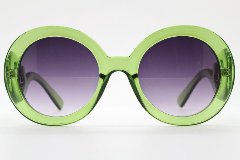 May include: Oversized round sunglasses featuring a translucent lime green plastic frame and dark gradient lenses that transition from a deep purple tint at the top to a lighter shade at the bottom, with visible hinges on the outer edges.