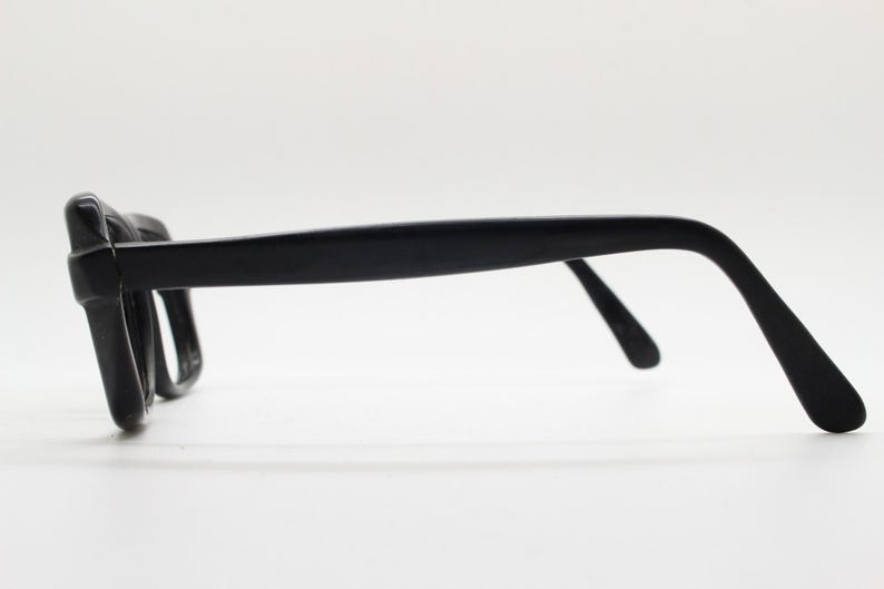 May include: Black plastic framed eyeglasses with a simple design. The glasses have a rectangular shape and are made of a lightweight material.