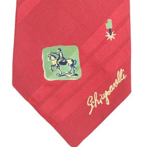 May include: Red tie with a diagonal striped pattern. Features a green square with a rider on a horse, a spur, and the name "Schiparelli" in cursive.