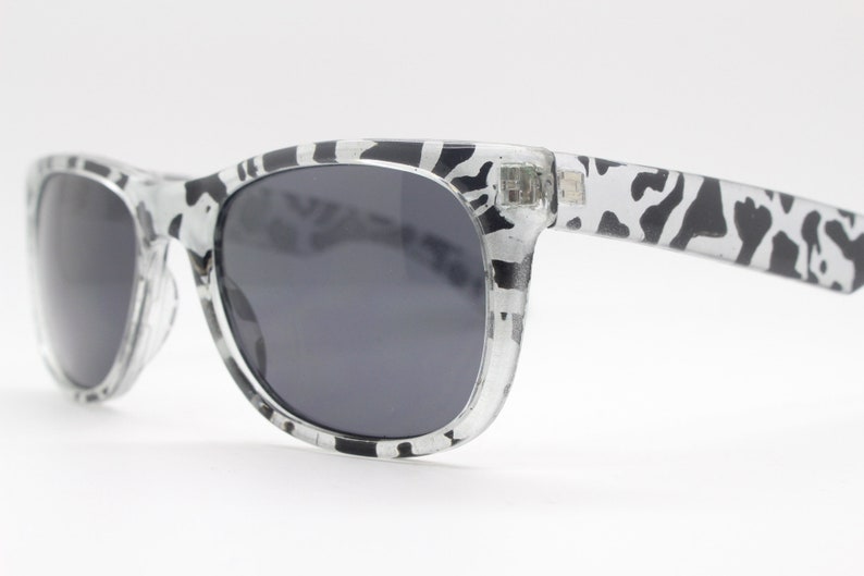 May include: Black and white patterned sunglasses with dark gray lenses. The sunglasses have a classic, rectangular shape.
