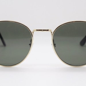 Pu&ograve; includere: Occhiali da sole rotondi con montatura in metallo dorato e lenti verde scuro. Il design classico presenta un doppio ponte e aste sottili. Questi occhiali offrono un look elegante per l'uso quotidiano.