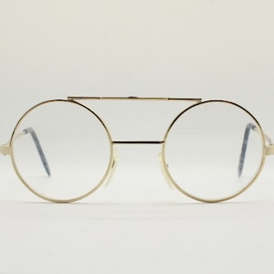 Puede incluir: Gafas redondas de metal dorado con puente fino y lentes transparentes.