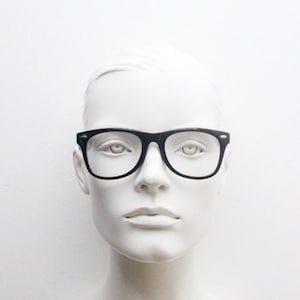 May include: A white mannequin head wearing black rectangular eyeglasses with a thin black frame.