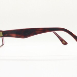 May include: A pair of tortoiseshell eyeglasses with purple tinted lenses. The glasses have a gold Ray-Ban logo on the side.