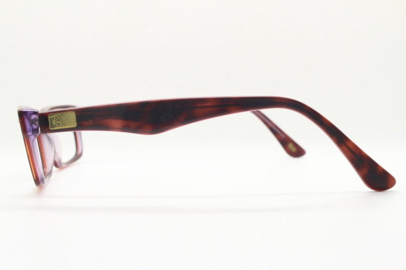 May include: A pair of tortoiseshell eyeglasses with purple tinted lenses. The glasses have a gold Ray-Ban logo on the side.