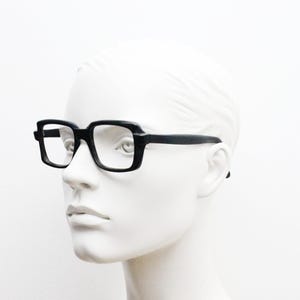 May include: Black rectangular eyeglasses with a thick frame and clear lenses.