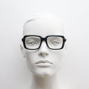 May include: A black plastic frame with rectangular lenses. The glasses are on a white mannequin head.