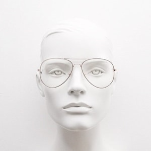 Könnte beinhalten: Ein weißer Mannequin-Kopf, der eine klare Aviator-Brille mit einem dünnen goldenen Rahmen trägt.