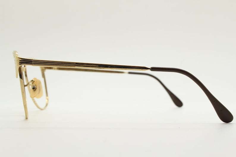 Puede incluir: Gafas de metal dorado con patillas de pl&aacute;stico marr&oacute;n. Las gafas tienen una montura rectangular y un puente de metal fino.