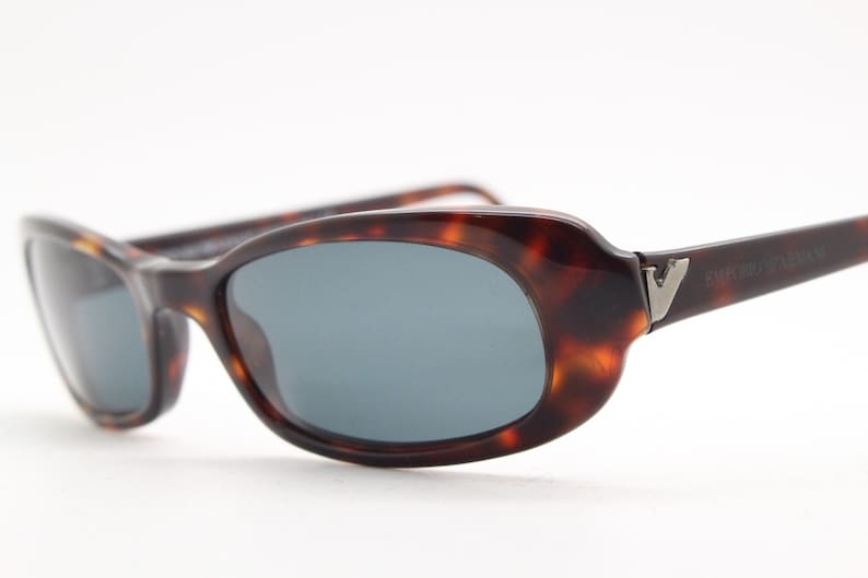 Op de afbeelding: Zonnebril met een schildpadpatroon en ovale glazen. De monturen zijn bruin met donkere accenten. De veren hebben een zilveren embleem en de merknaam "EMPORIO ARMANI".