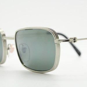 May include: Silver-toned square-shaped sunglasses with green lenses. The sunglasses have a thin metal frame with a subtle textured design.