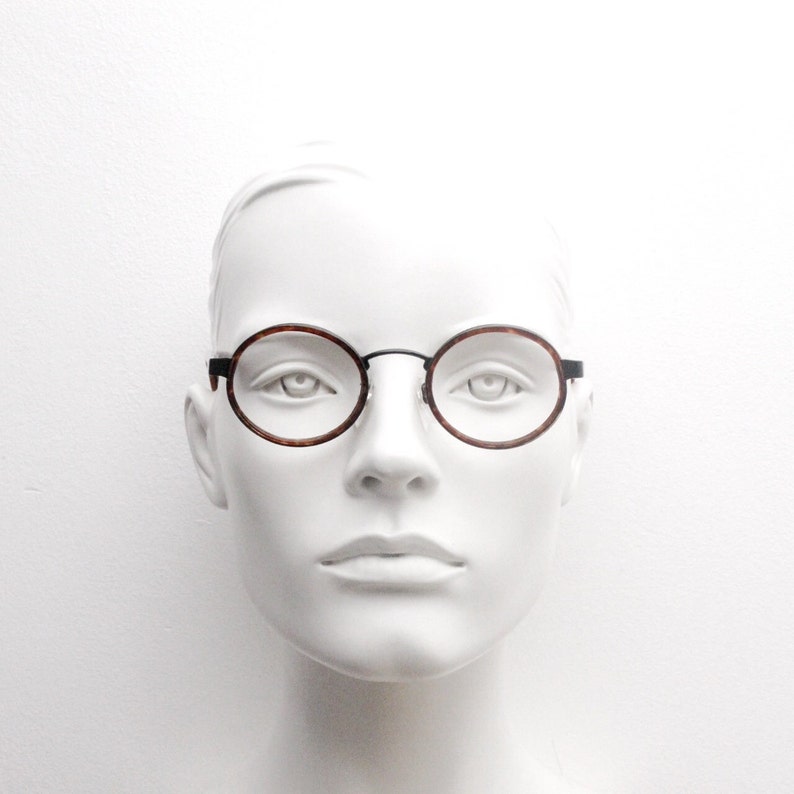 May include: A white mannequin head wearing round, tortoiseshell-framed glasses with black metal accents.
