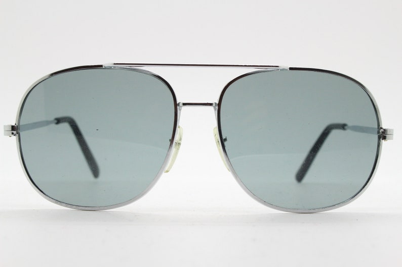 May include: Silver aviator sunglasses with gray lenses. The sunglasses have a thin metal frame and a double bridge.