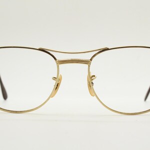 Puede incluir: Gafas de metal doradas con montura cuadrada redondeada y lentes transparentes.