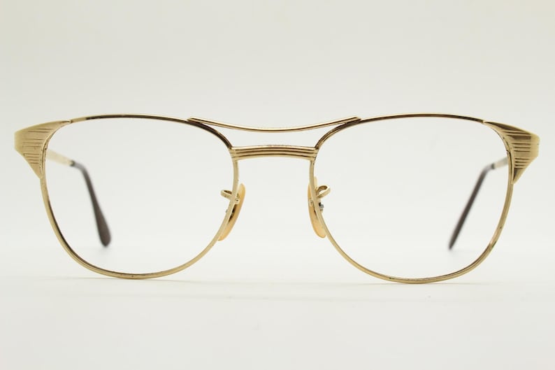 Puede incluir: Gafas de metal doradas con montura cuadrada redondeada y lentes transparentes.