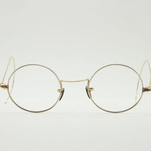 Peut inclure: Lunettes en métal doré dotées de montures circulaires fines et d'un pont délicat. La paire comprend des branches fines et incurvées conçues pour se placer derrière les oreilles, ainsi que de petites plaquettes nasales réglables.
