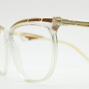 Könnte beinhalten: Transparente Kunststoffbrille im Cat-Eye-Stil mit goldfarbenem und braunem Gestell.