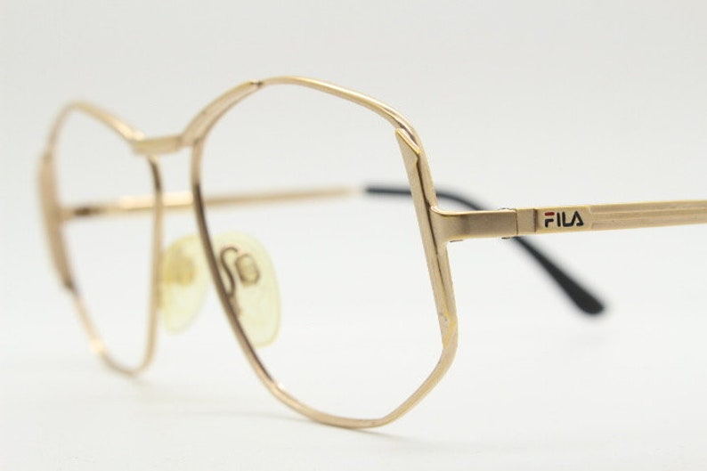Puede incluir: Gafas de metal doradas con montura de forma geom&eacute;trica y la palabra "FILA" impresa en el lateral.