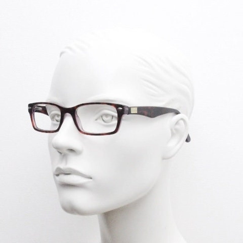 May include: A brown and tortoiseshell patterned eyeglasses frame with clear lenses. The frame has a gold accent on the side.