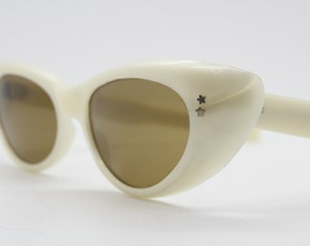 Könnte beinhalten: Weiße Cat-Eye-Sonnenbrille mit braunen Gläsern und zwei silbernen Stern-Akzenten am rechten Gestell.
