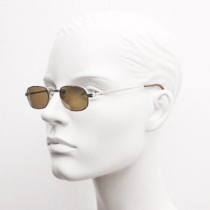May include: Silver frame sunglasses with brown lenses. The sunglasses are on a white mannequin head.