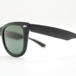 Puede incluir: Gafas de sol negras con un dise&ntilde;o cl&aacute;sico y retro. Las monturas son gruesas y mate, con un peque&ntilde;o acento plateado en las patillas. Las lentes tienen un tinte verde, ofreciendo un contraste elegante. Un accesorio atemporal.