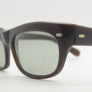 May include: A pair of brown tortoiseshell sunglasses with green lenses. The sunglasses have a classic cat-eye shape and are in good condition.