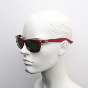 May include: Red Ray-Ban sunglasses with green lenses. The sunglasses are on a white mannequin head.