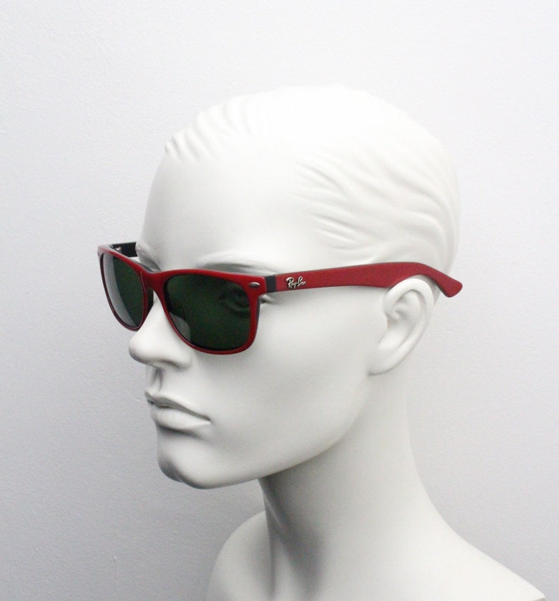 May include: Red Ray-Ban sunglasses with green lenses. The sunglasses are on a white mannequin head.