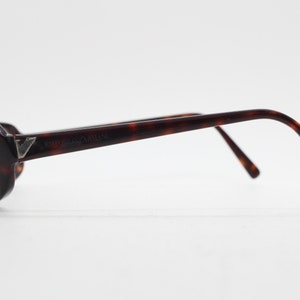 Op de afbeelding: Emporio Armani zonnebril met een schildpadpatroon. De zonnebril heeft donkere glazen en een zilveren logo op het montuur. De pootjes buigen naar de oren.