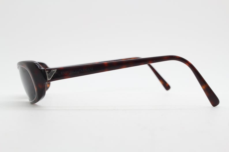Op de afbeelding: Emporio Armani zonnebril met een schildpadpatroon. De zonnebril heeft donkere glazen en een zilveren logo op het montuur. De pootjes buigen naar de oren.