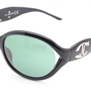May include: Black oval sunglasses with green lenses and a silver "Just Cavalli" logo on the right lens. The sunglasses have a black frame with a silver "JC" logo on the right arm.