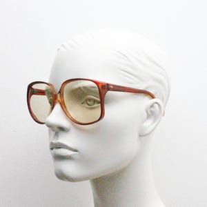 Op de afbeelding: Vintage oversized vierkante bril met een roodbruin montuur en getinte glazen. De bril heeft een klassiek retro-ontwerp, perfect voor een gedurfde fashion statement. De monturen zijn dik en stevig.