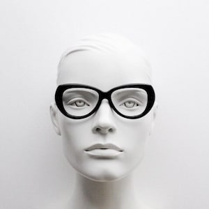 May include: A white mannequin head wearing black cat-eye glasses.