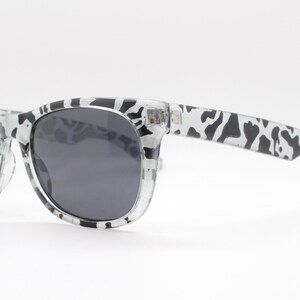 May include: Black and white patterned sunglasses with dark gray lenses. The sunglasses have a classic, rectangular shape.