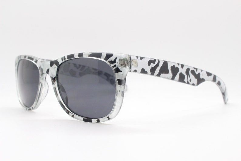 May include: Black and white patterned sunglasses with dark gray lenses. The sunglasses have a classic, rectangular shape.