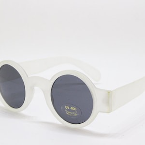 May include: White round sunglasses with dark gray lenses. The sunglasses have a UV 400 and impact resistant label on the right lens.